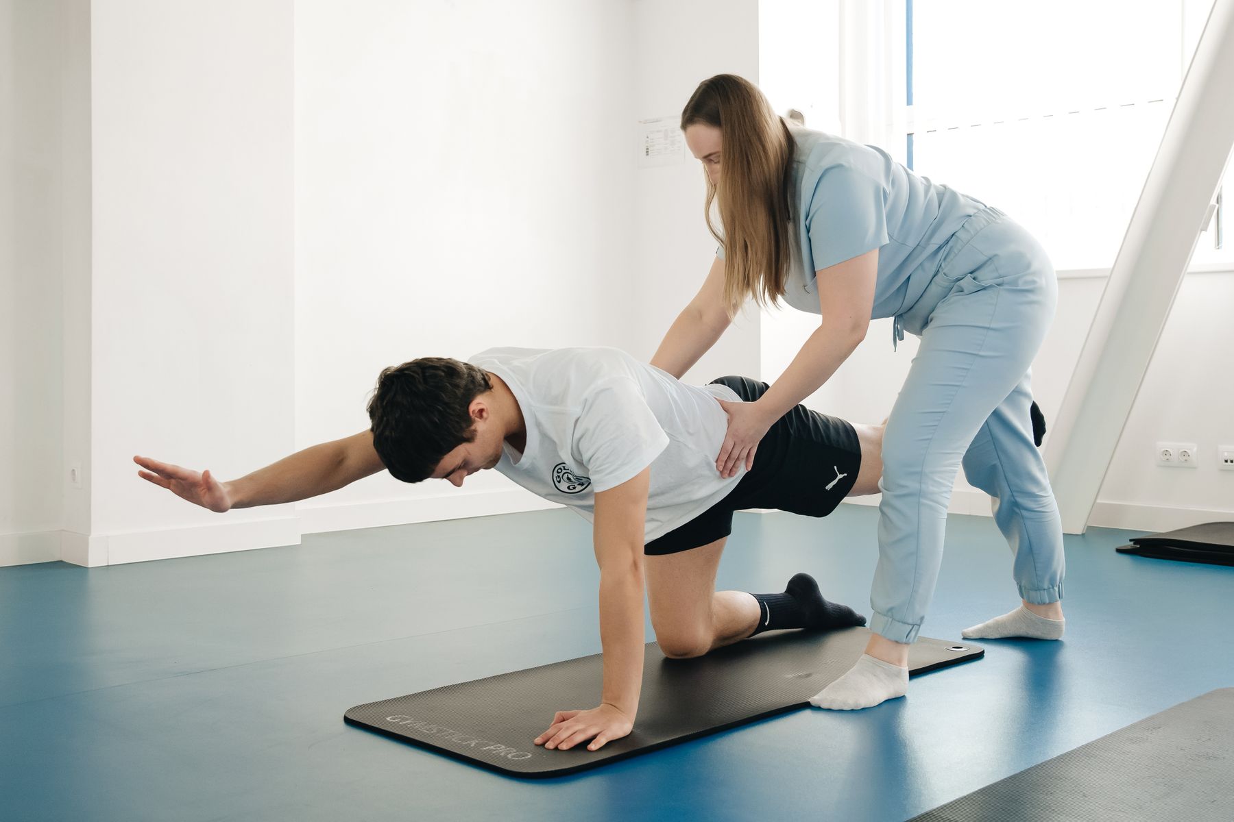 Physiotherapist supporting a patient's exercise on a mat